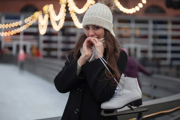 Young brunette with skates on her shoulder, on a background of winter city Park — Stock Photo, Image