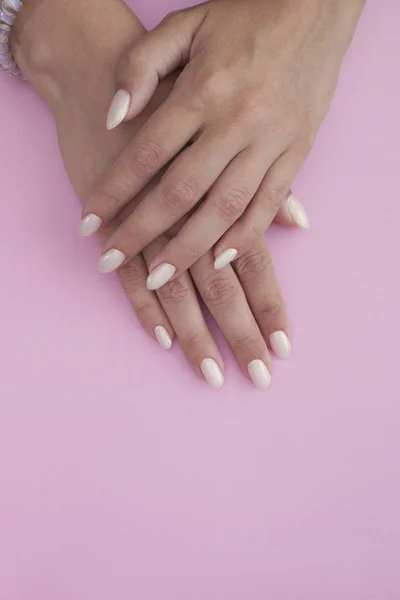 Tanned hands of a young woman with a light manicure on a pink background. Nail Polish — Stock Photo, Image