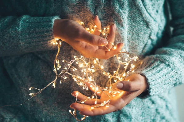 Luci nei palmi delle mani. Le mani delle donne tengono una ghirlanda. Ragazza in un maglione blu con le luci di Natale nelle sue mani — Foto Stock