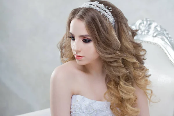 Jovem noiva encantadora com penteado de luxo. Mulher bonita em vestido de noiva sentado em uma cadeira . — Fotografia de Stock