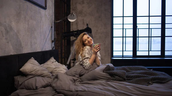 Chica se despertó temprano en la mañana y bebe café en la cama —  Fotos de Stock