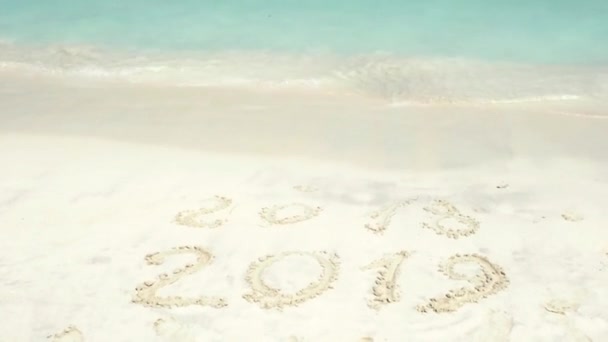2018 είναι τέλος 2019 έρχονται επιγραφή πάνω στην άμμο. Ένα μπλε κύμα έρχεται στην ξηρά. — Αρχείο Βίντεο