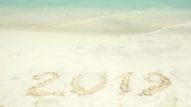 2018 is end 2019 is come inscription on the sand. A blue wave is coming ashore. — Stock Video