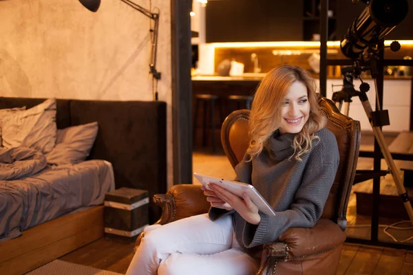 Vacker och självsäker ung blondin sitter i en mysig stol i hennes lägenhet. — Stockfoto