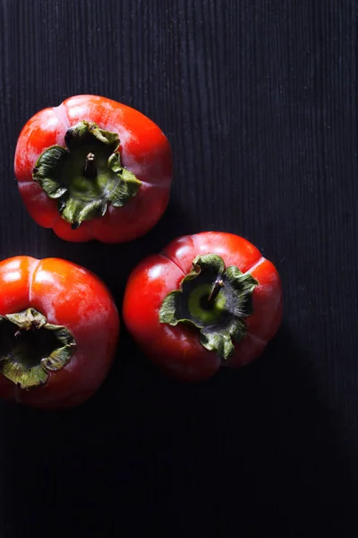 Fresh juicy persimmon on the black wooden background — Stock Photo, Image