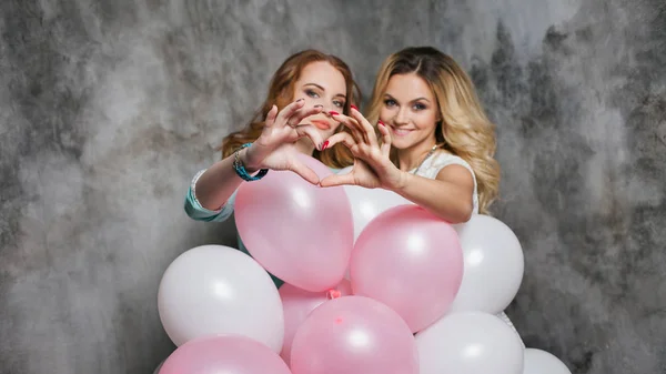 Blonde and redhead. Two young charming girlfriends at the party. Show sign heart. — Stock Photo, Image