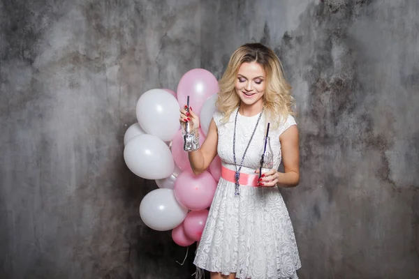 Young woman dancing and drinking soda. Portrait of a beautiful glamorous blonde, with a bottle of drink and balloons. — Stock Photo, Image