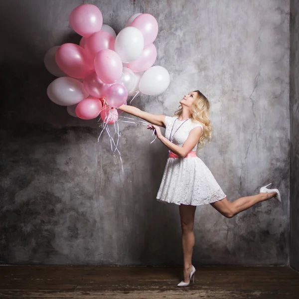 Encantadora jovem loira em um vestido branco com balões rosa, voar na festa. Menina feliz e alegre com balões . — Fotografia de Stock