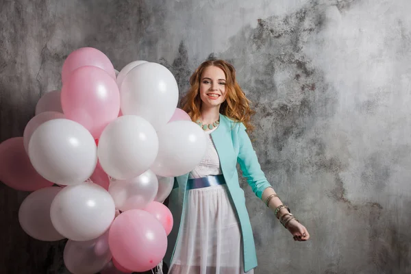 Red-haired beauty young woman in a white dress, holding a large bundle of balloons