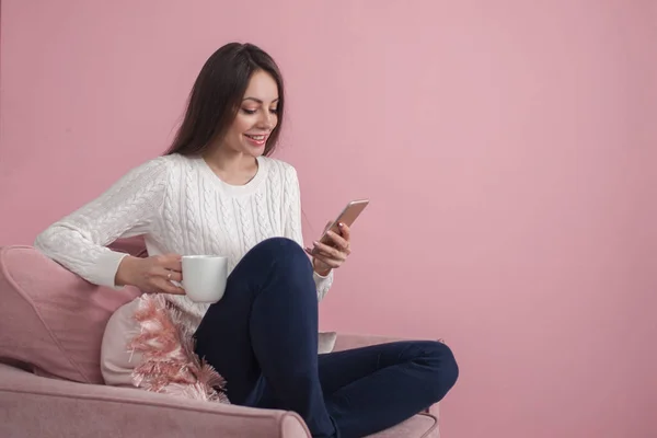 Charmante junge Brünette sitzt auf einem Stuhl und chattet mit einem Smartphone — Stockfoto