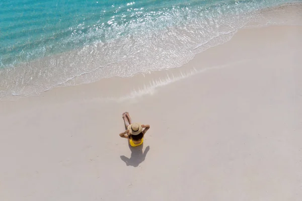Дівчина одна на березі моря і насолоджується сонцем. Молода жінка в солом'яному капелюсі і жовтому купальнику — стокове фото