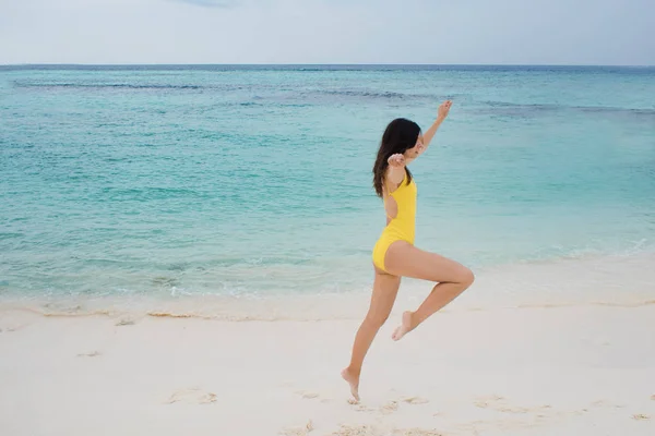 在海滩上跳黄色泳衣的苗条的黑发女孩. — 图库照片