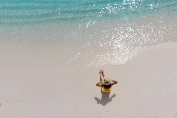 Girl alone on seashore and enjoys the sun. Young woman in a straw hat and yellow swimsuit — Stock Photo, Image