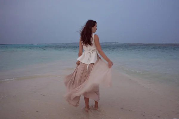 Back view of young woman against a sea horizon. Brunette girl in white skirt flying on wind