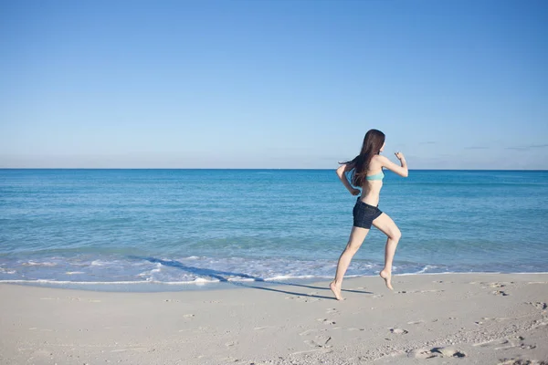 Jovem mulher de shorts correndo na praia — Fotografia de Stock