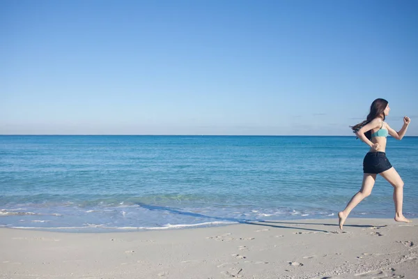 Mladá žena v šortkách běžící na pláži — Stock fotografie
