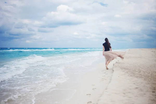 Zadní pohled na mladou ženu v dlouhé sukni, chůze na oceánu. — Stock fotografie