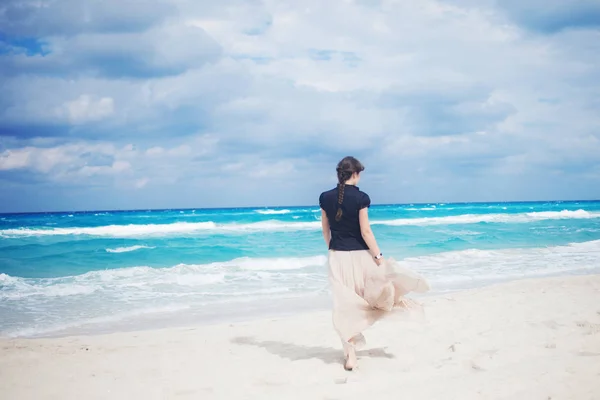 Back view of young woman in a long skirt walking on the ocean. — Stock Photo, Image