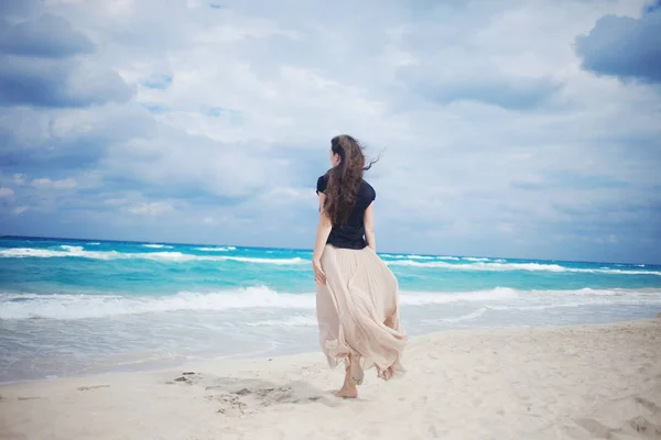 Back view of young woman in a long skirt walking on the ocean. — Stock Photo, Image