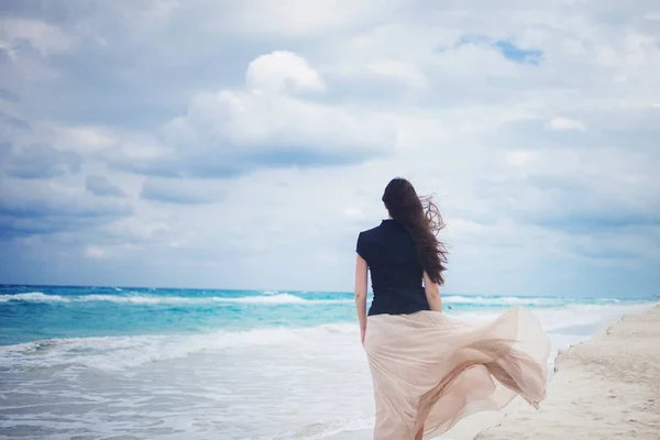 Back view of young woman in a long skirt walking on the ocean. — Stock Photo, Image