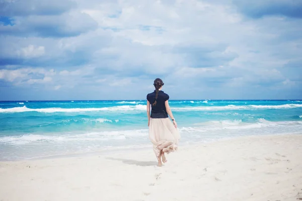 Back view of young woman in a long skirt walking on the ocean. — Stock Photo, Image