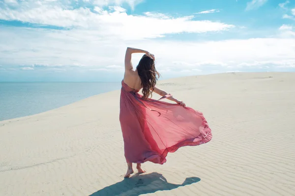 Woman in red waving dress with flying fabric runs on background of dunes. — Stock Photo, Image