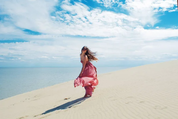 Mujer en vestido ondulante rojo con tela voladora se ejecuta en el fondo de las dunas . — Foto de Stock