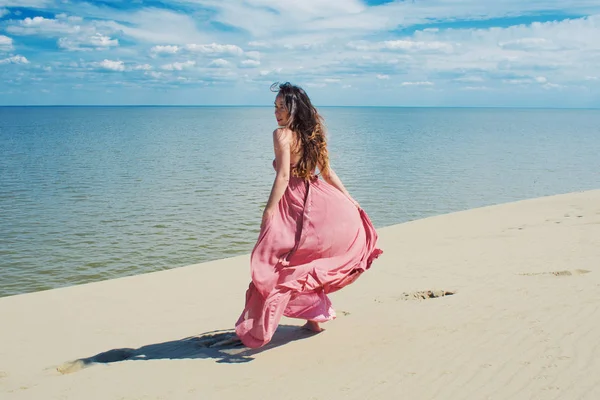 Femme en robe rouge ondulée avec tissu volant fonctionne sur fond de dunes . — Photo