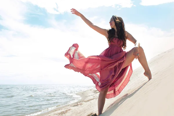 Woman in red waving dress with flying fabric runs on background of dunes. — Stock Photo, Image