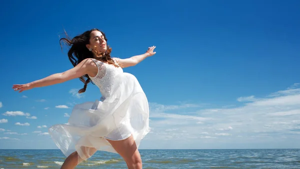 Young beautiful jumping brunette woman in white dress — Stock Photo, Image