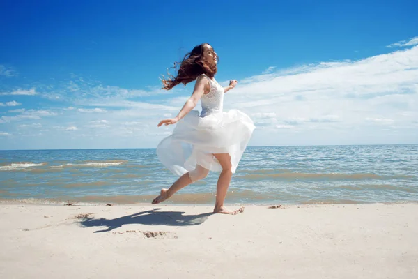 Jonge mooie springen brunette vrouw in witte jurk — Stockfoto
