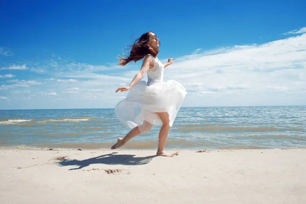 Young beautiful jumping brunette woman in white dress — Stock Photo, Image