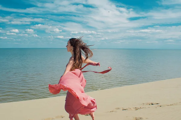 Vrouw in rode jurk met vliegende stof zwaaien draait op de achtergrond van duinen. — Stockfoto