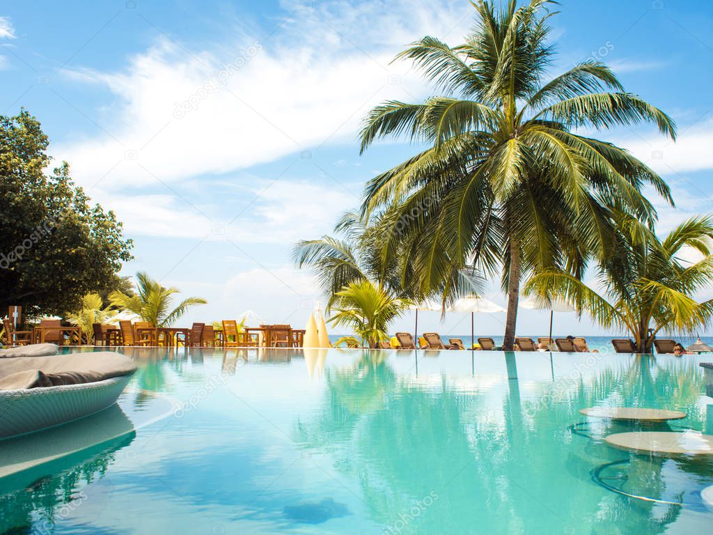 Blue water in the swimming pool and fluffy palm trees. Luxury resort on tropical iseland.