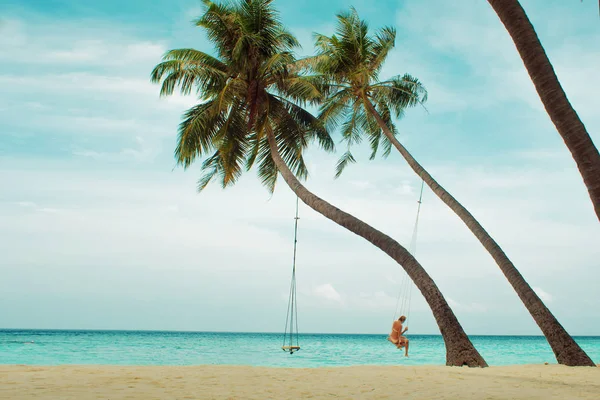 Swing on a palm tree. Beautiful island landscape with relaxing girl on a swing.