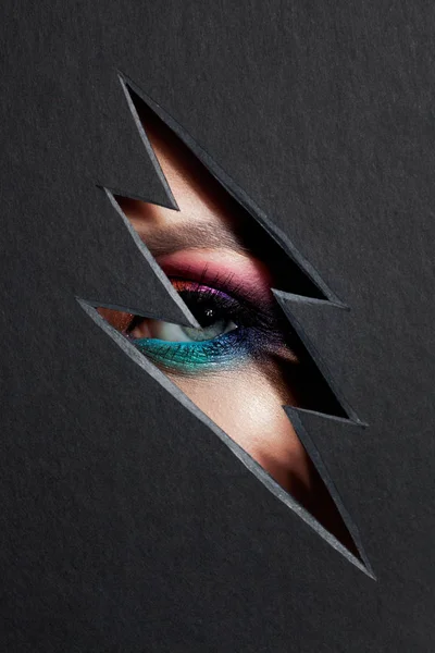 Beautiful female eye with color makeup. Cutout in paper in the form of a lightning. — Stock Photo, Image