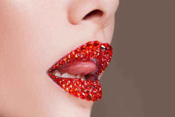 Red lips covered with rhinestones. Beautiful woman with red lipstick on her lips