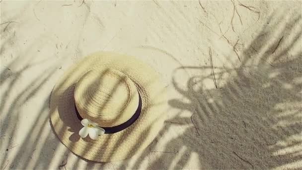 Strohhut auf Sand, Sonnenschutzkonzept. Stillleben mit Hut und Palmblättern — Stockvideo