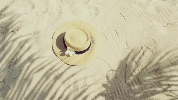 Straw hat on sand, sun protection concept. Still life with a hat and shades of palm leaves — Stock Video