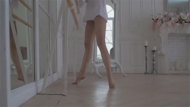 Όμορφη νεαρή γυναίκα στο παράθυρο σε ένα λευκό πουκάμισο. χορό και χαλάρωση στην αίθουσα χορού στο μπαλέτο Barre — Αρχείο Βίντεο