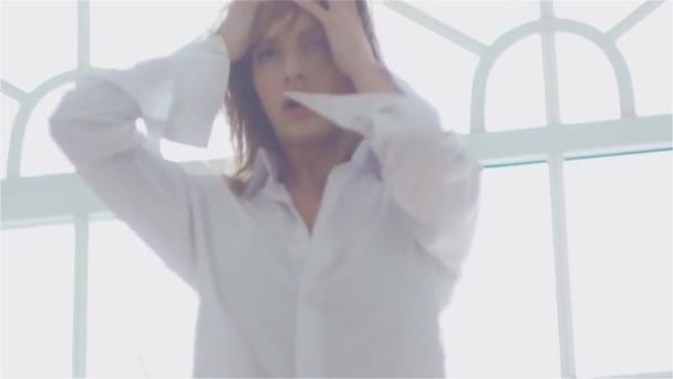 Красивая молодая женщина у окна в белой рубашке. танцы и отдых — стоковое видео