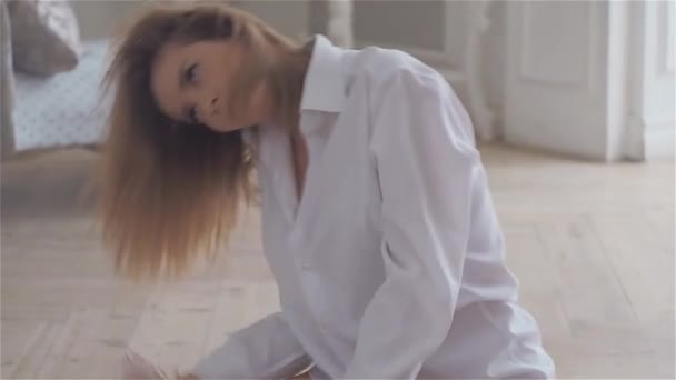 Μια όμορφη νεαρή γυναίκα σε ένα λευκό πουκάμισο κάθεται στο πάτωμα στη μεγάλη αίθουσα. — Αρχείο Βίντεο