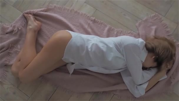 Beautiful young woman in a white shirt is lying on the floor. — Stock Video