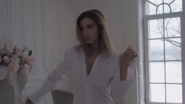 Όμορφη νεαρή γυναίκα στο παράθυρο σε ένα λευκό πουκάμισο. χορό και χαλάρωση — Αρχείο Βίντεο