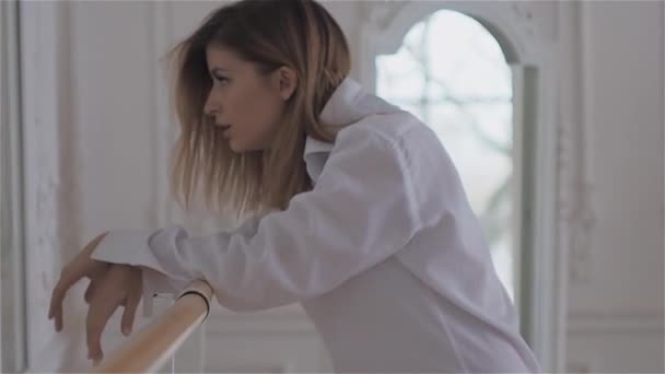 Hermosa joven en la ventana con una camisa blanca. bailando y relajándose en la sala de baile del ballet Barre — Vídeo de stock