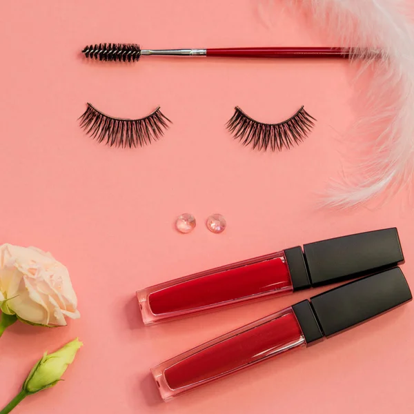 Eyelashes, powder eyebrow brush and lipstick as a beautiful face, concept on pink background.