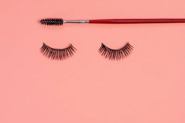 Eyelash extension, concept. Women's eyelashes and brush for styling and combing eyebrows on a pink background — Stock Photo, Image