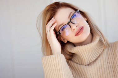 Gözlüklü ve bej kazaklı genç, sevimli bir sarışın. Modaya uygun genç bir kadın..