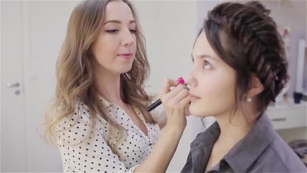 Vacker brunett flicka använder tjänster av en professionell makeup artist. Skönhetssalong. Make-up artist och hennes klient — Stockvideo