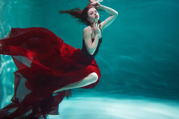 Bella giovane donna in un abito rosso nuota sott'acqua — Foto Stock